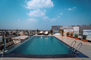 A rooftop pool with lounge chairs, potted plants, and a city view. - Aura Inn & Suites (Mysore)