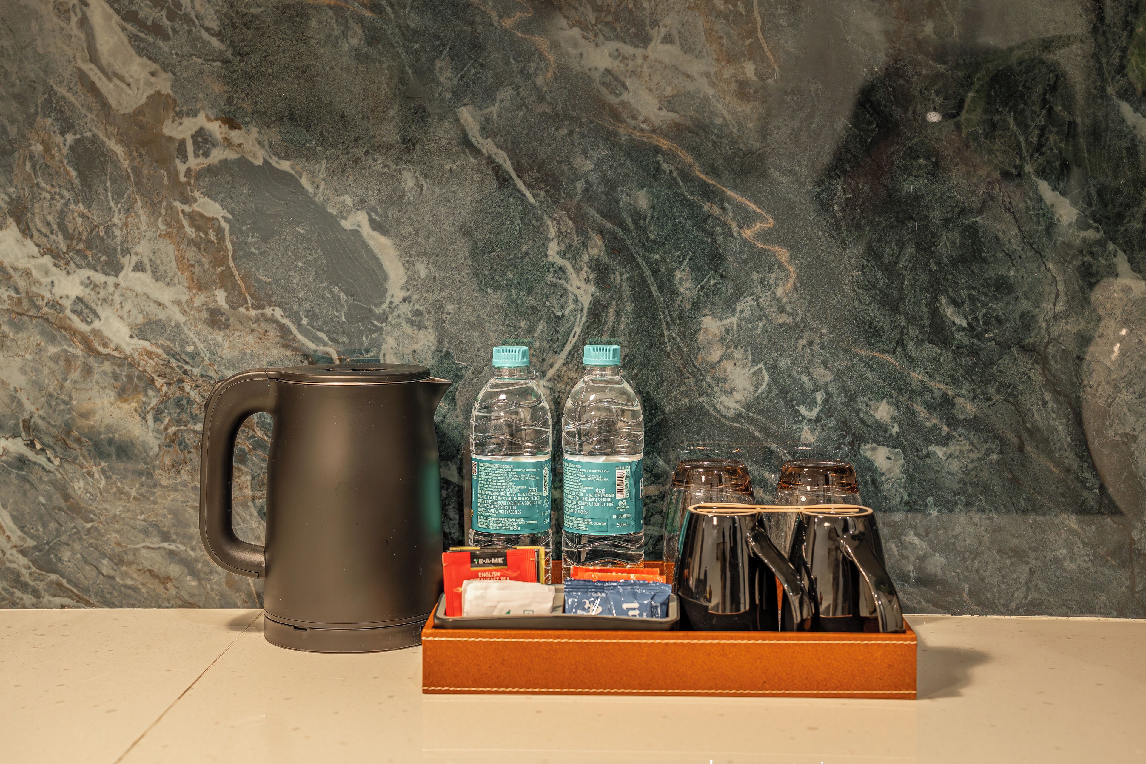 A coffee maker, two water bottles, a box with toiletries, and a mug on a countertop.