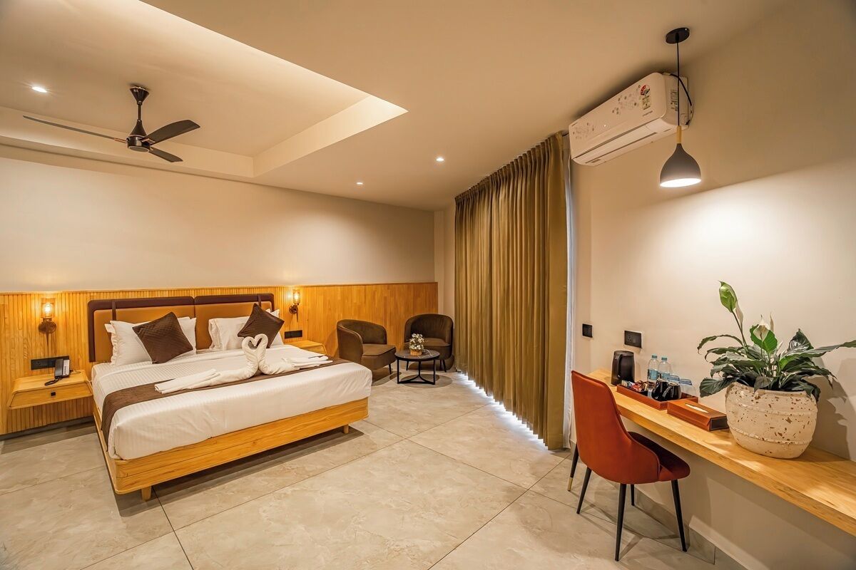 Habitación de hotel con cama, dos sillas, un escritorio, una planta en maceta y un equipo de aire acondicionado.