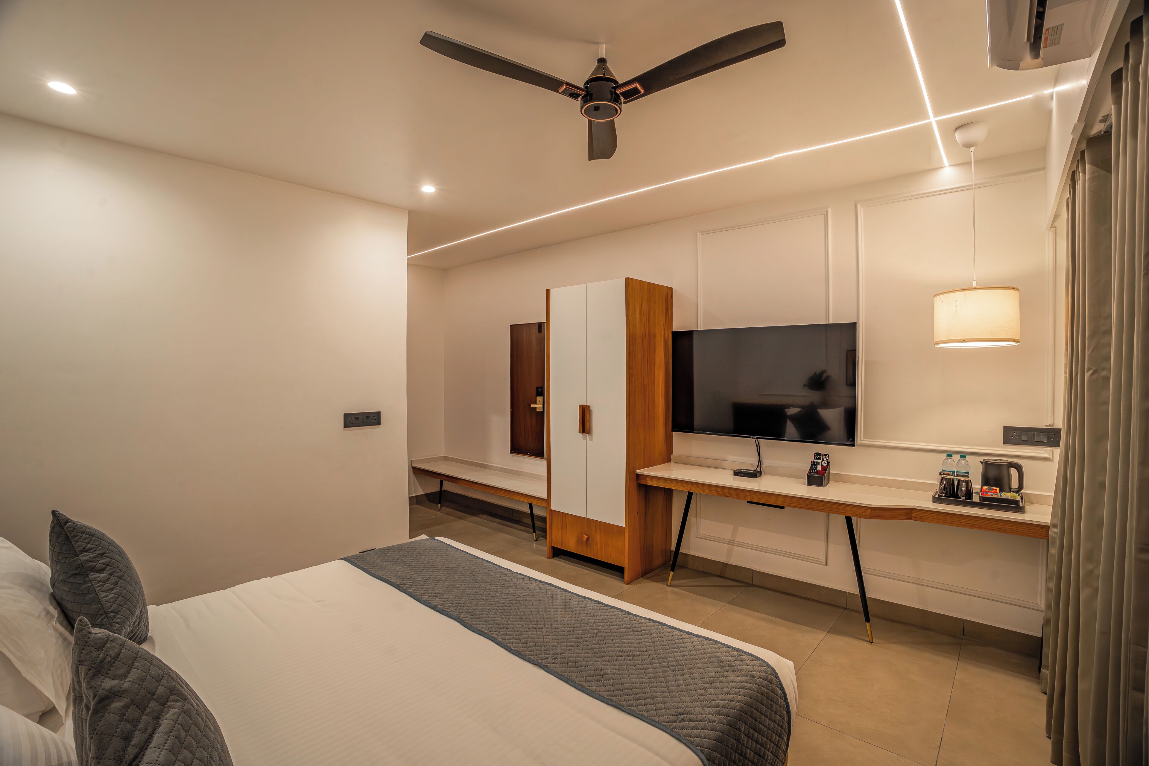 Una habitación de hotel con cama, escritorio con televisor, armario y ventilador de techo.