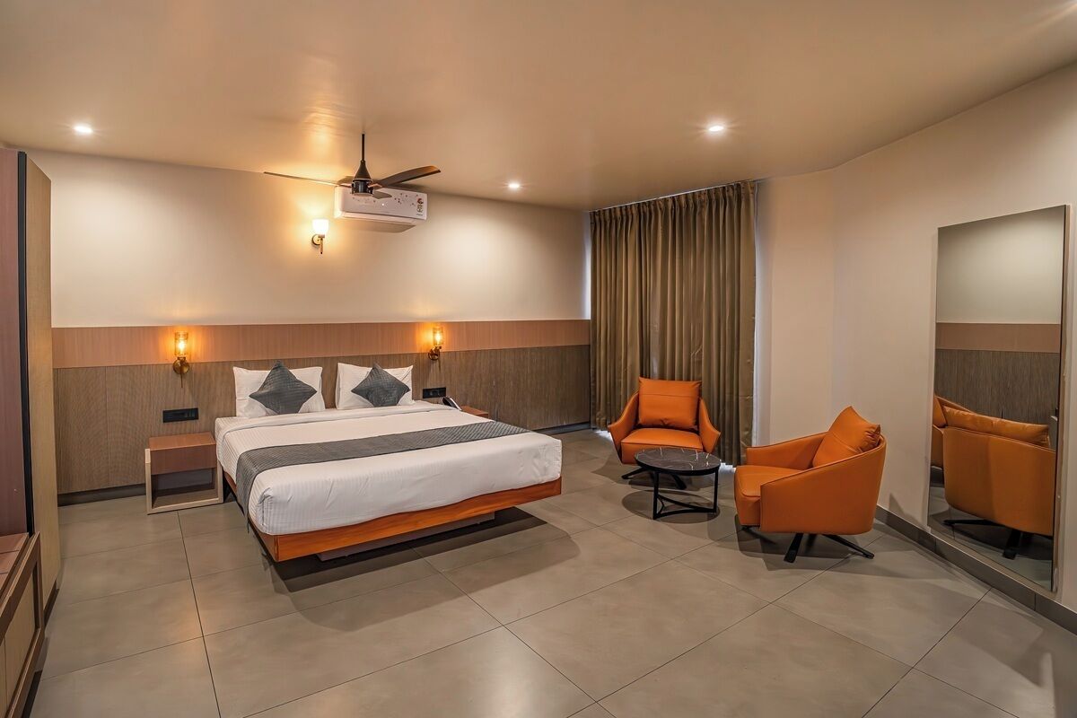 A hotel room with a bed, two chairs, a small table, a ceiling fan, and wall-mounted lights.