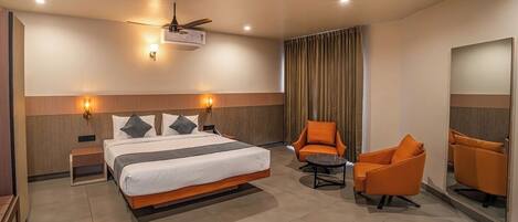 A hotel room with a bed, two chairs, a small table, a ceiling fan, and wall-mounted lights.