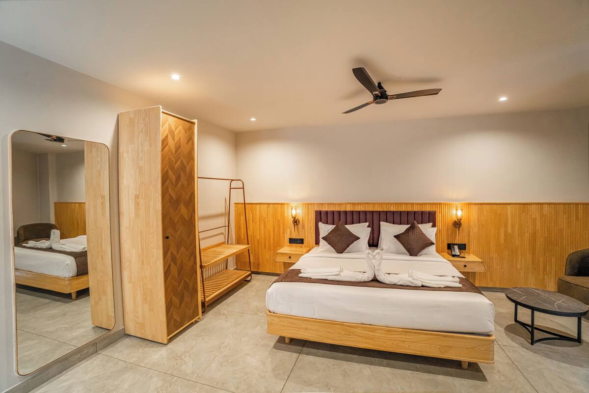 Quarto de hotel moderno com uma cama grande, um ventilador de teto, um guarda-roupa de madeira e uma pequena mesa.