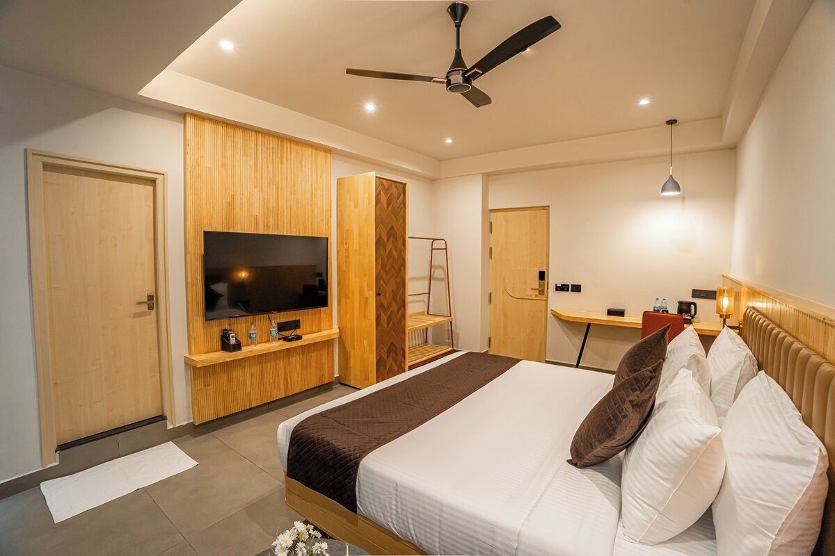 A modern hotel room with a bed, television, wooden paneling, a desk, and a ceiling fan.