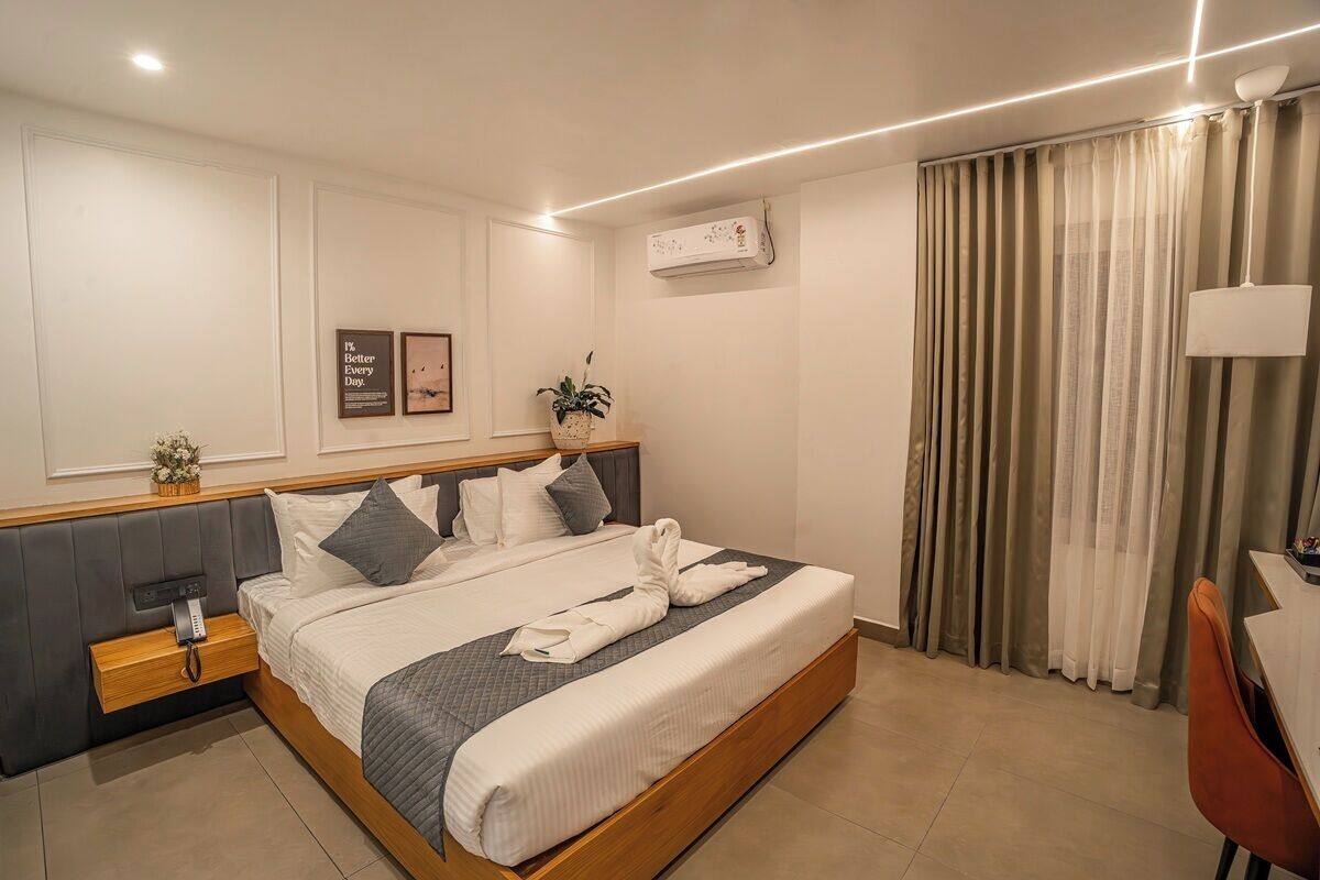 Quarto de hotel com cama, mesa de cabeceira, luminária, cortinas e ar condicionado fixado na parede.