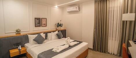A hotel room with a bed, bedside table, lamp, curtains, and a wall-mounted air conditioner.