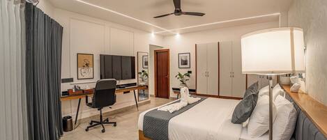 Une chambre d’hôtel équipée d’un lit, d’un bureau, d’une chaise, d’une télévision, d’une armoire et d’un ventilateur de plafond.
