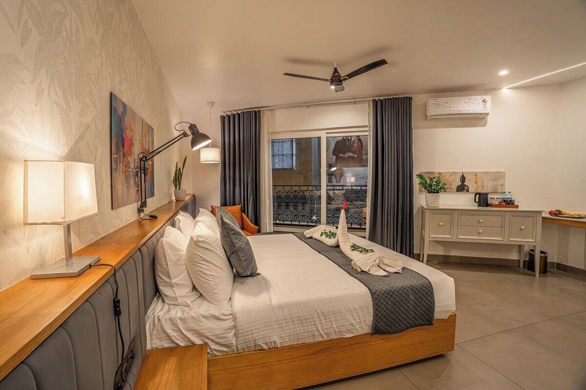 Quarto de hotel moderno com cama, mesa de cabeceira, luminária e vista para a varanda.
