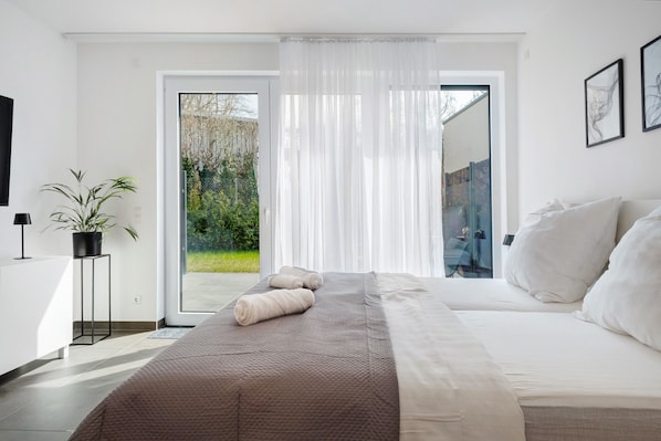 Une chambre moderne avec un grand lit, une plante en pot et une vue à travers une porte vitrée.