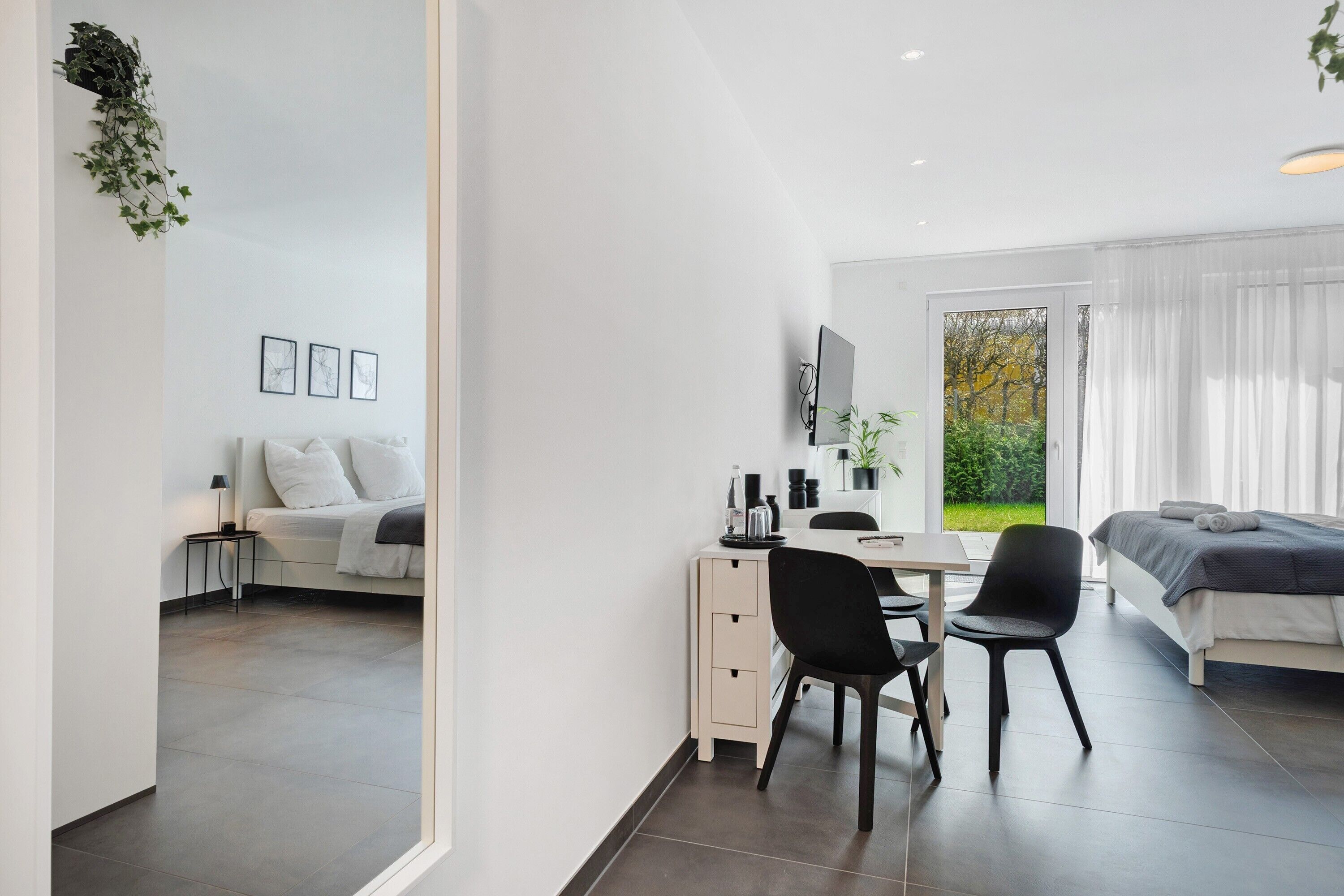 Ein modernes Zimmer mit einem Bett, Schreibtisch, Stuhl, einem kleinen Tisch und einem Fenster mit Vorhängen.