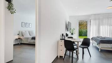 Ein modernes Zimmer mit einem Bett, Schreibtisch, Stuhl, einem kleinen Tisch und einem Fenster mit Vorhängen.