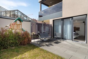 A modern house with a patio, a play structure, and a visible bedroom with a bed.