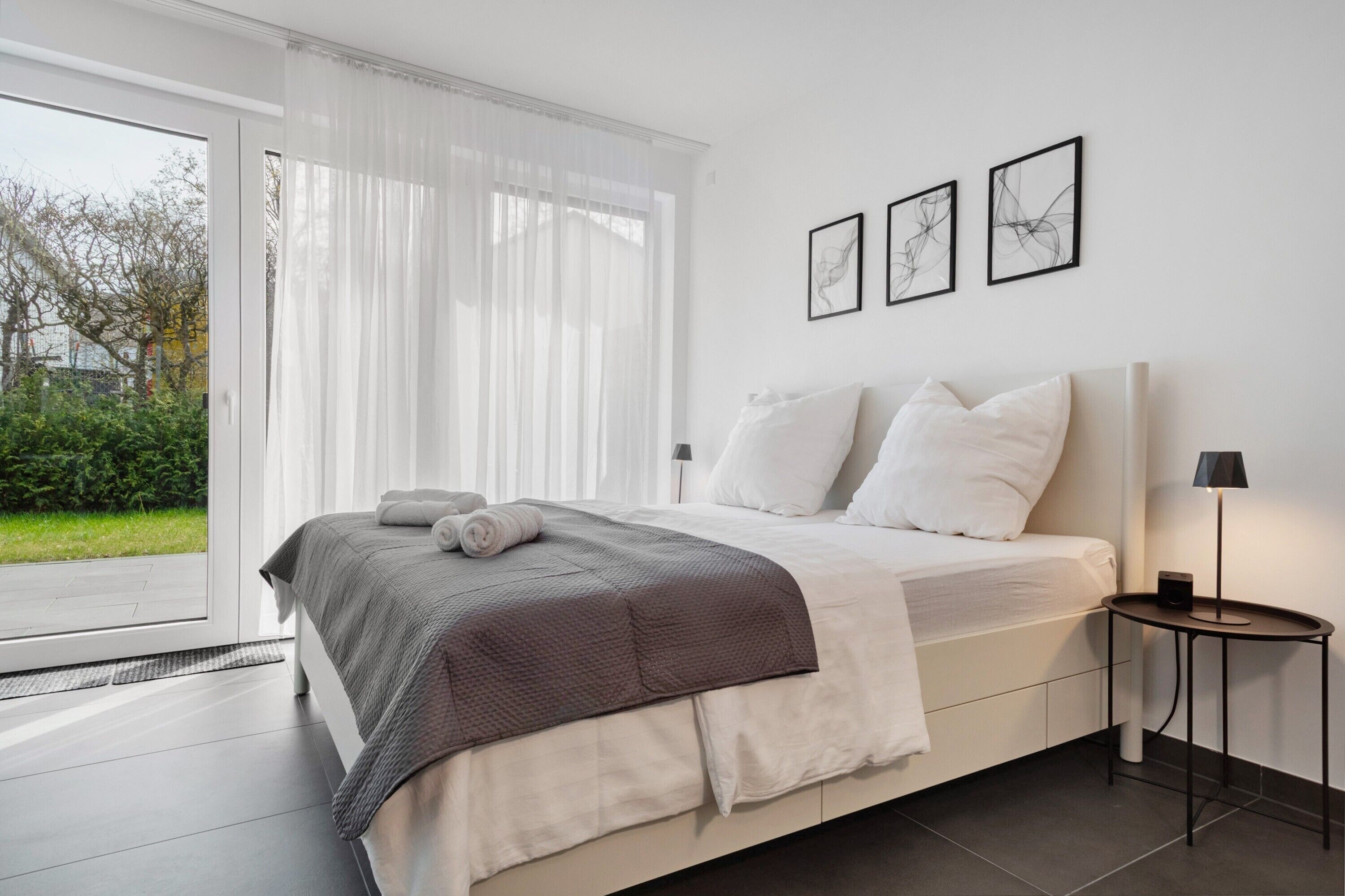 A modern bedroom with a bed, a bedside table with a lamp, and a view through a glass door.
