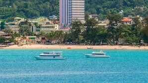A coastal cityscape with a prominent hotel, a mountain with a temple, and boats on the water. - The Cozy Beach Front Hotel (Patong)