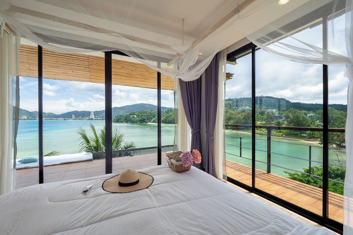 A bedroom with a large window, a bed, a hat, and a basket with flowers.