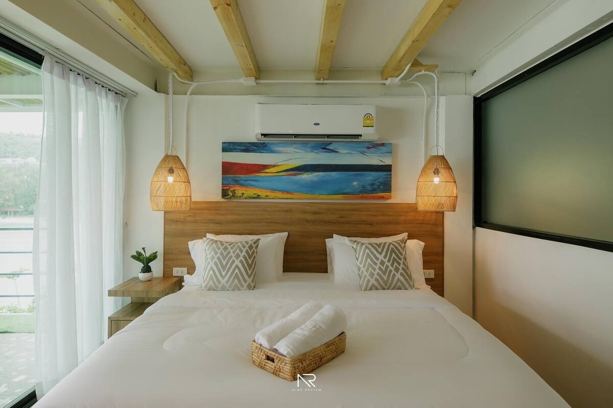 A hotel room with a bed, two bedside lamps, a painting, and an air conditioning unit.