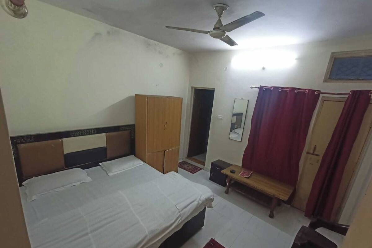 A bedroom with a bed, a wardrobe, a ceiling fan, a mirror, and a door with curtains.
