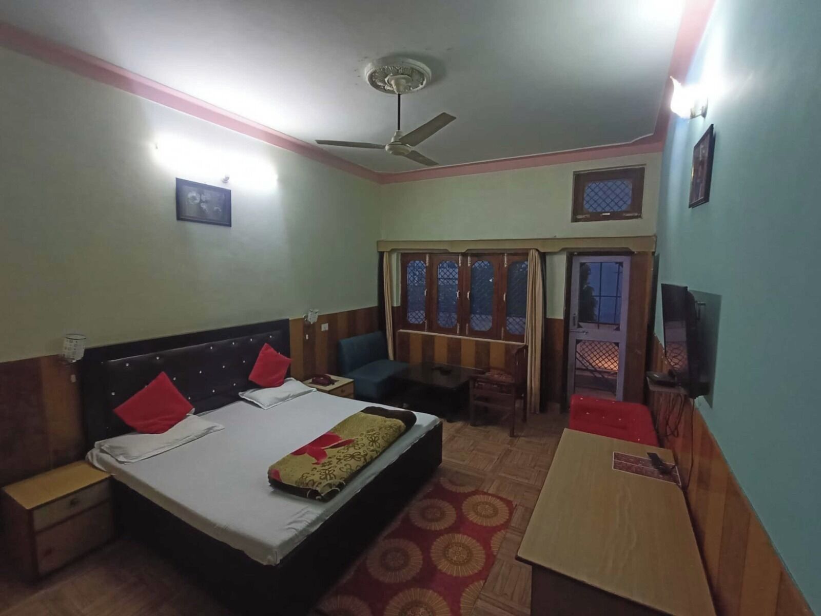 A hotel room with a bed, a desk, a chair, a ceiling fan, and a window with a view.