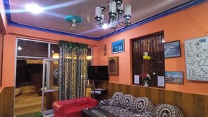 Una sala de estar con un sofá, una butaca roja, una mesa de centro, un televisor y una araña.