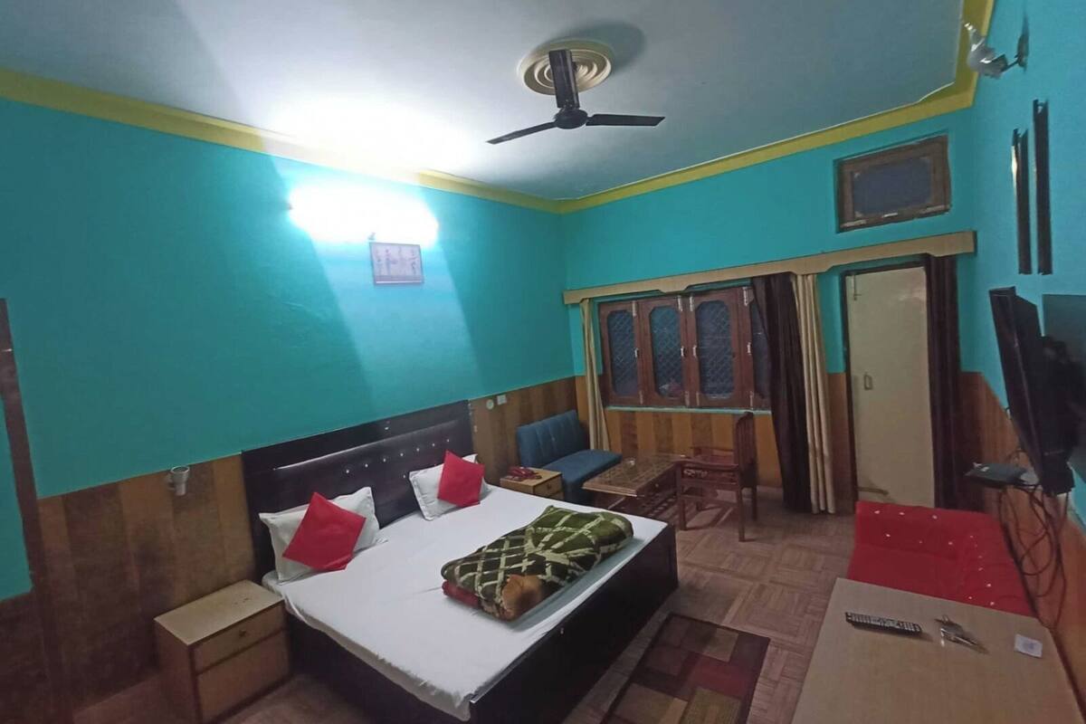 A room with a bed, bedside tables, a desk, a chair, a wardrobe, a ceiling fan, and a television.