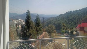 Un balcón con vistas a un paisaje montañoso, un edificio de techo rojo y cielo despejado.