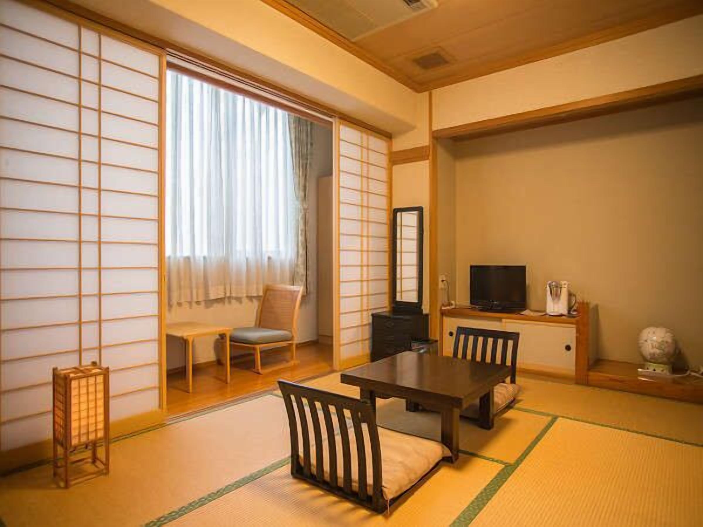 A traditional Japanese room with tatami flooring, a low table, chairs, a television, and sliding doors.