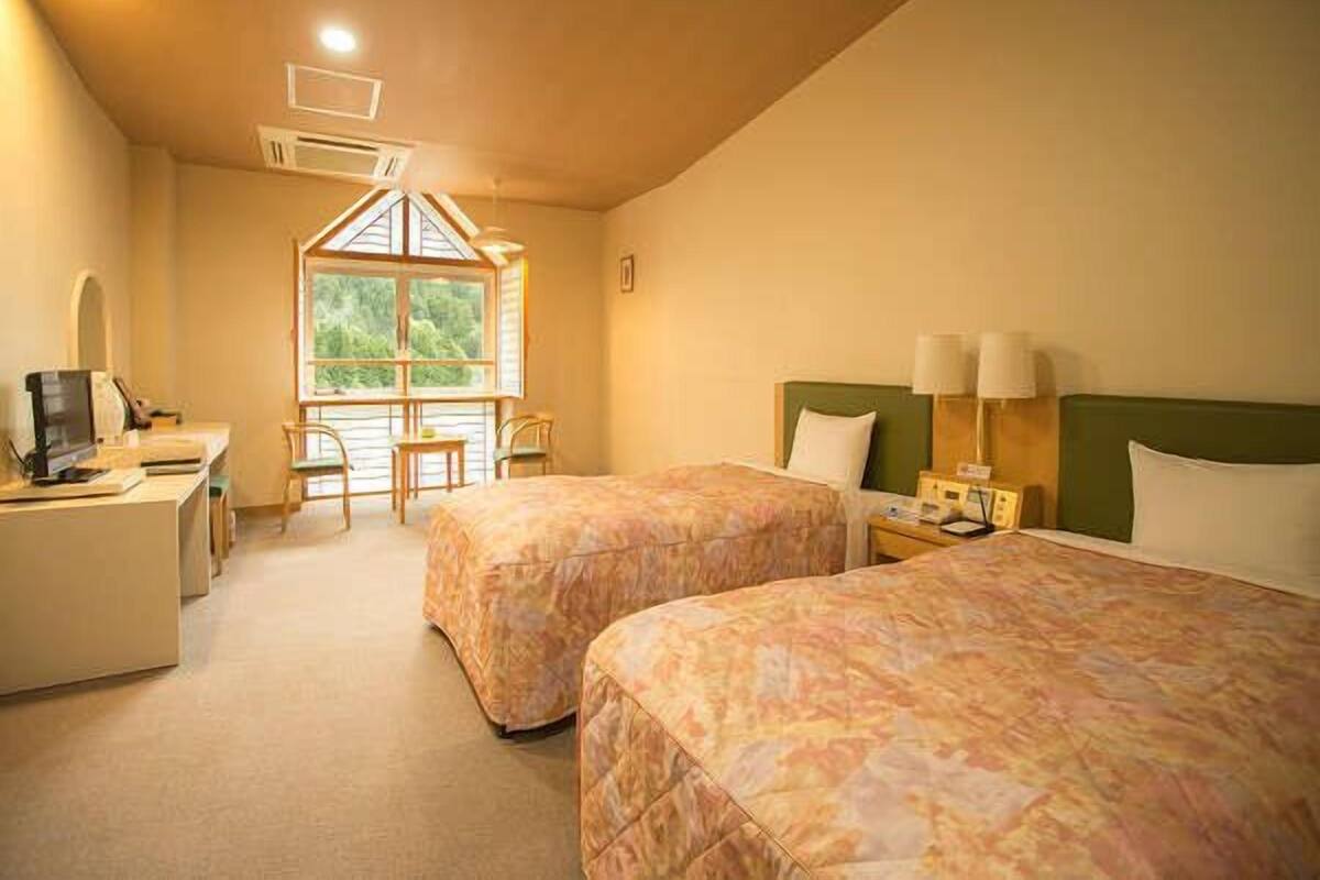 A hotel room with two beds, a desk with a computer, a window with a view, and a small table with chairs.