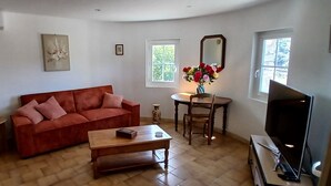 Un soggiorno con un divano rosso, un tavolino in legno, una TV, un piccolo tavolino rotondo con un vaso di fiori e una finestra vista verde.