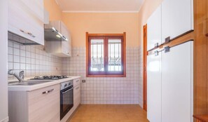 A compact kitchen with white cabinets, a gas stove, a sink, and a window.