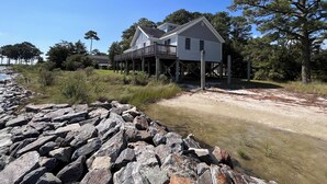 A house with a deck, surrounded by natural landscape and a rocky shoreline. - 4BR Riverfront Stilt Home w/ Panoramic Views & Private Beach in Gloucester, VA (Gloucester)