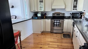 A kitchen with wooden flooring, white cabinets, stainless steel appliances, and a red chair. - 4BR Riverfront Stilt Home w/ Panoramic Views & Private Beach in Gloucester, VA (Gloucester)