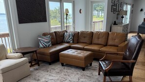 A spacious living room with a sectional sofa, a chaise lounge, a wooden floor, and large windows offering a view of the outdoors. - 4BR Riverfront Stilt Home w/ Panoramic Views & Private Beach in Gloucester, VA (Gloucester)
