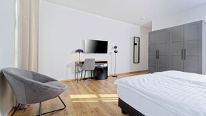 A modern hotel room with a bed, a desk with a chair, a television, and a wardrobe. - Boardinghouse Rosenheim (Rosenheim)