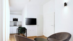 A modern living room with a dining area, a flat-screen TV, and a kitchen in the background. - Boardinghouse Rosenheim (Rosenheim)