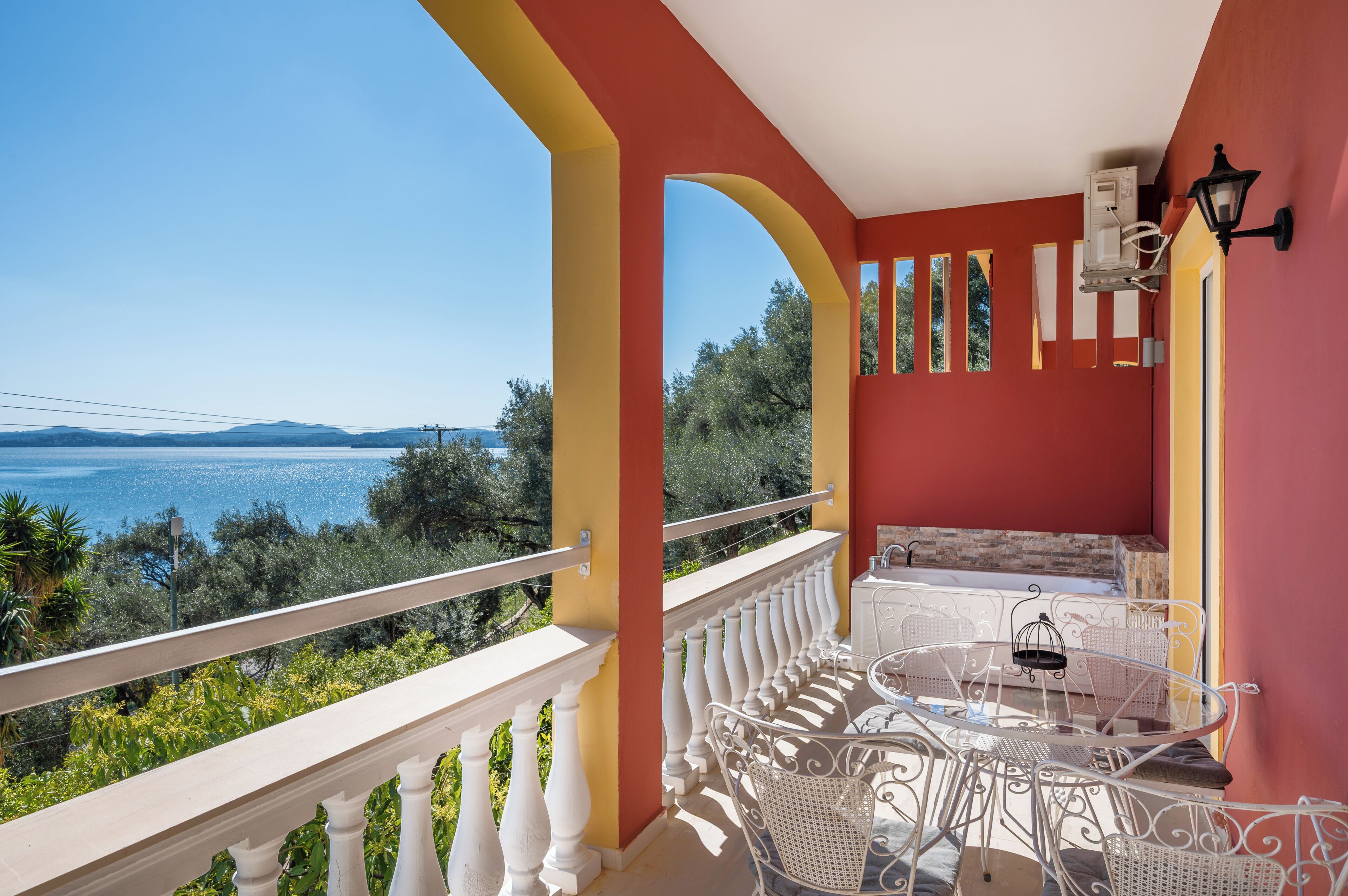 A balcony with a view of the sea, white balustrades, and a table with chairs.