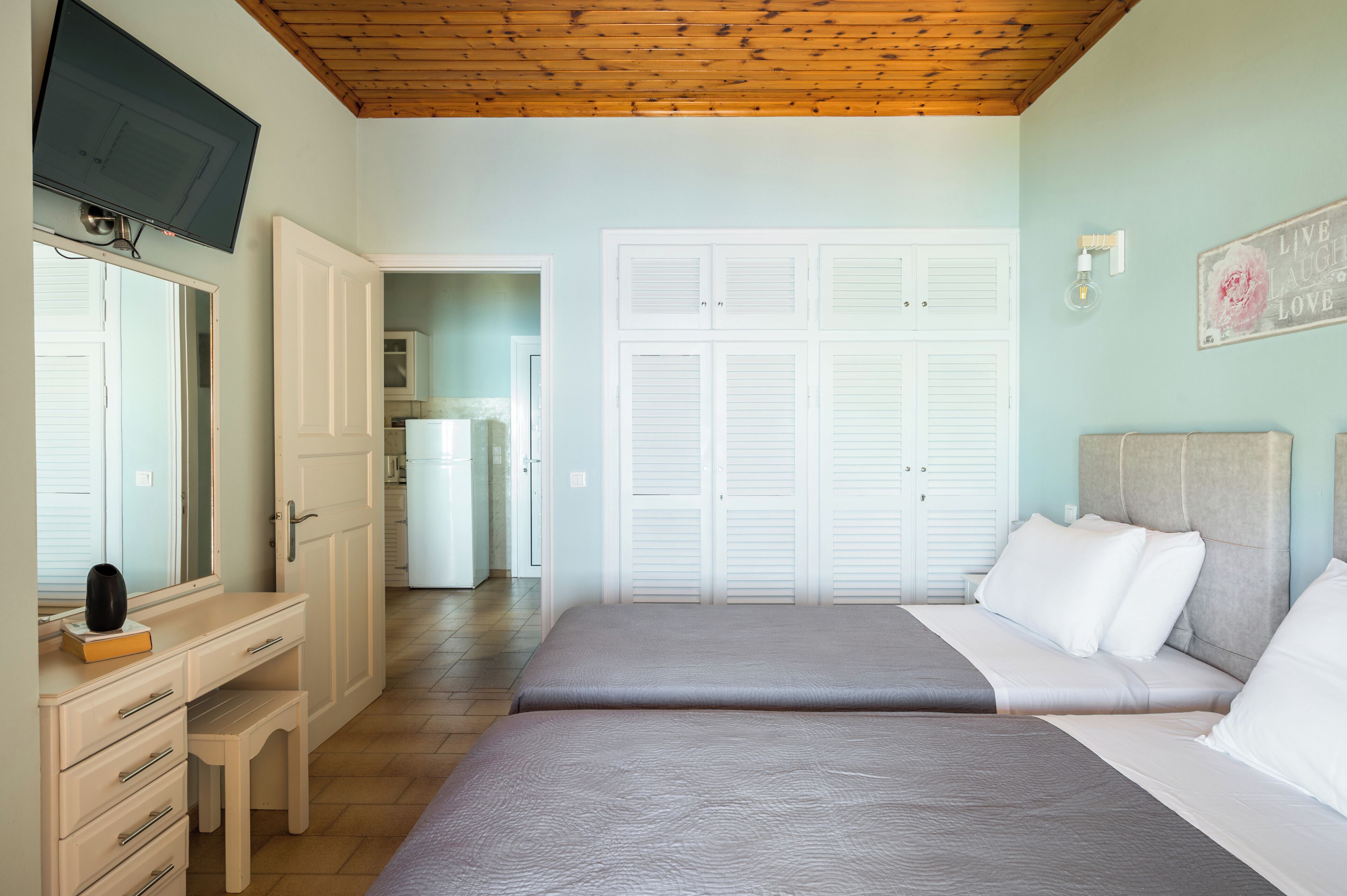 A bedroom with two beds, a desk, a television, and a wardrobe.