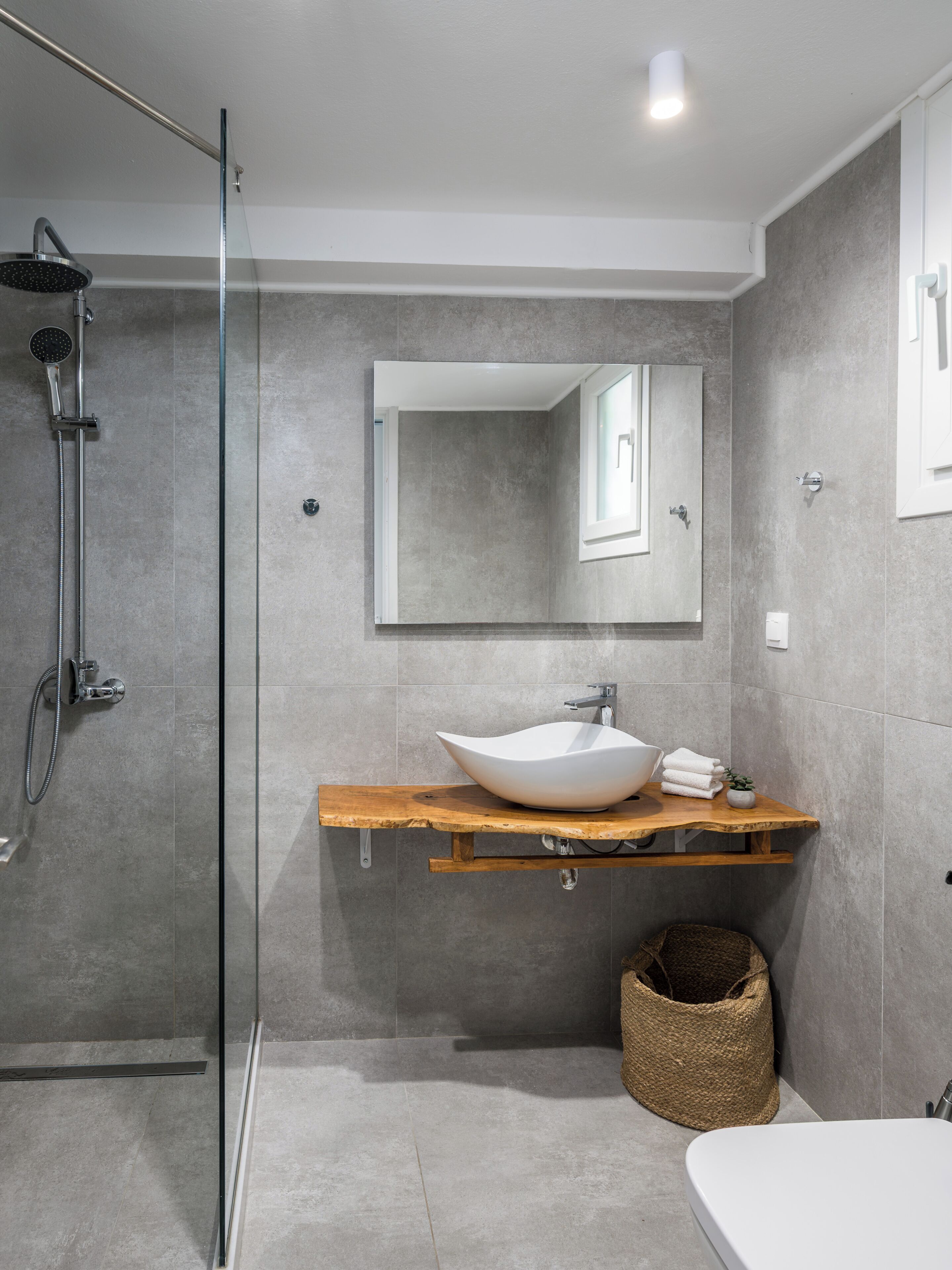 A modern bathroom with a glass shower enclosure, a wooden vanity with a white vessel sink, and a large mirror.