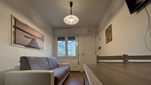 Una habitación moderna con sofá, suelo de madera, luz de techo, ventana con persianas y puerta.