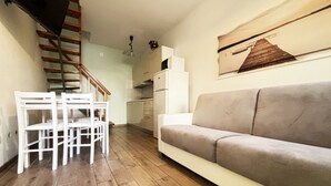 Una sala de estar con un sofá, una mesa de comedor con sillas, un área de cocina y una escalera.