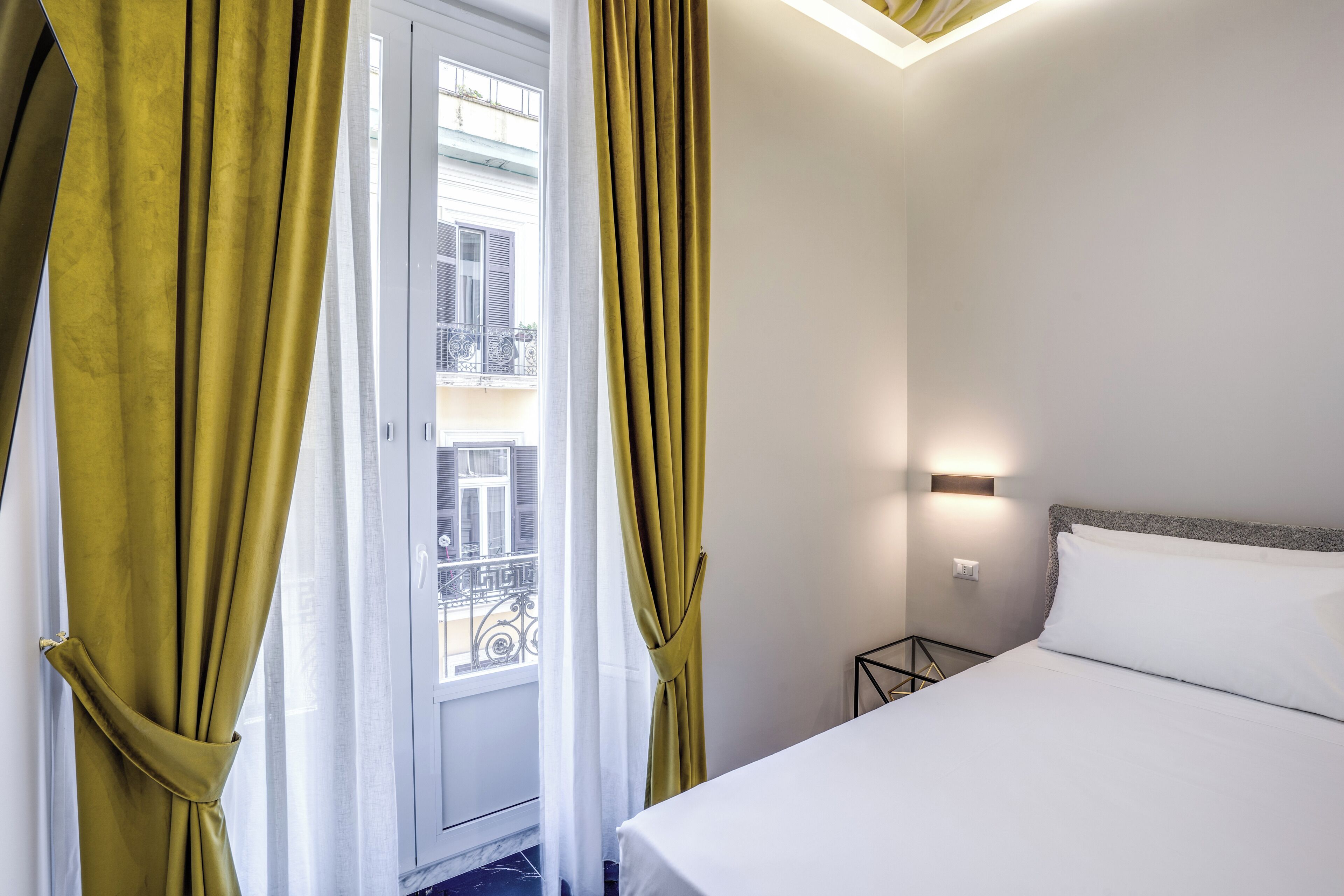 Hotellihuone, jossa on sänky, verhot, yöpöytä ja ikkuna, josta on näkymä parvekkeelle.