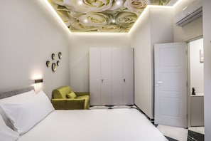 A modern bedroom with a bed, a green armchair, a wardrobe, and a door. - Lady Rose One (Naples)