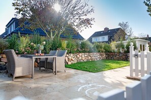 Une terrasse dotée de meubles en osier, d’un mur en pierre et d’une clôture en bois peinte en blanc.