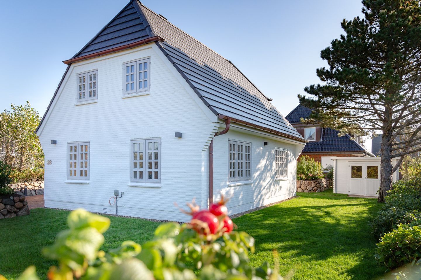 A white house with a steep roof, a small attached garage, and a well-maintained lawn.