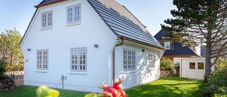 A white house with a steep roof, a small attached garage, and a well-maintained lawn.