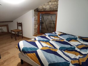 A bedroom with a bed, a chair, a stone wall, and a door. - La Tourterelle – Charming Barn in the Heart of Quercy (Saint-Georges)