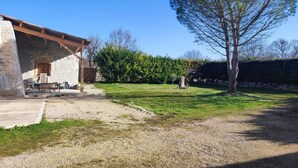 A stone building with a wooden roof, outdoor seating, and a large tree in the yard.