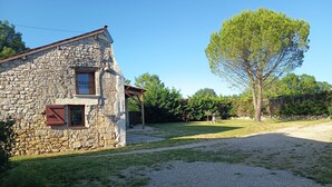 A stone house with a gravel driveway, a covered porch, and a large tree in the yard.