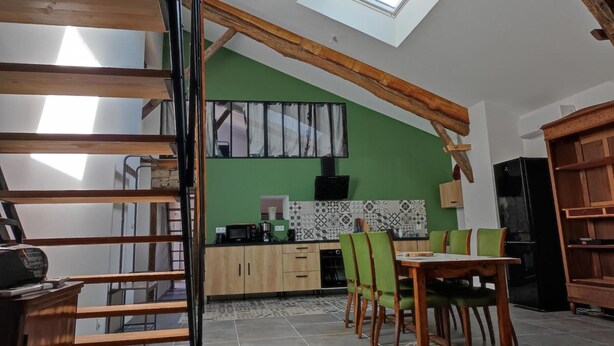 A loft-style room with a skylight, wooden beams, a kitchen with green walls, and a dining area with a table and chairs.