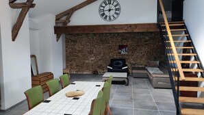A dining area with a wooden table and chairs, a stone wall, a clock, and a staircase.