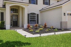 A residential building with a front entrance, a landscaped garden, and a driveway. - Modern 5BR  Family Getaway w/ Pool close to Disney (Clermont)